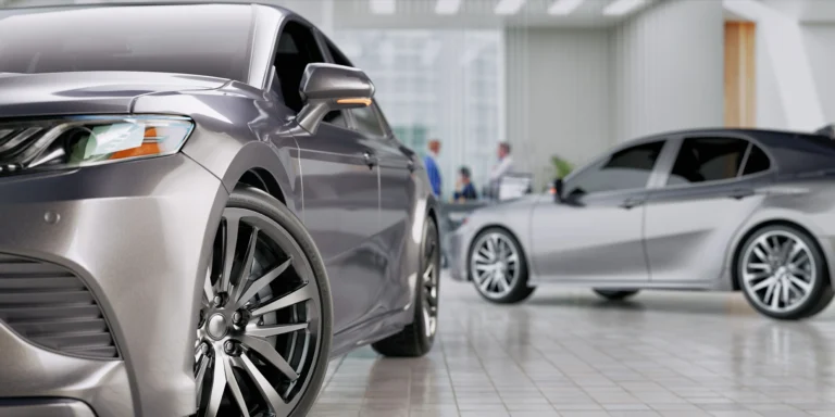 Close-up of two silver luxury sedans displayed in a modern showroom with blurred people in the background.
