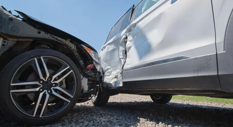 Two vehicles involved in a collision, showing front-end and side damage under clear sky.