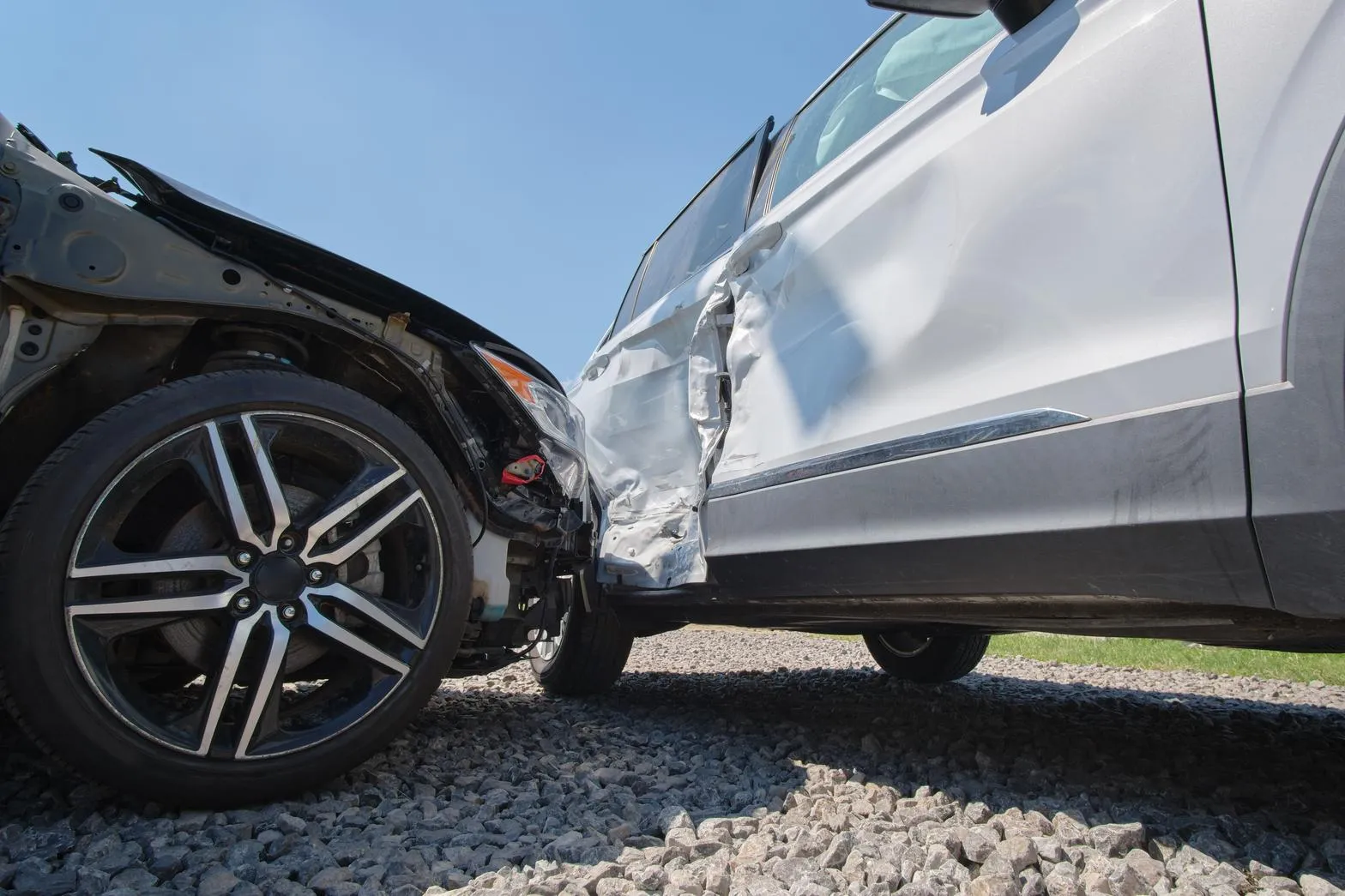 Two collision-damaged vehicles, a black car and a silver SUV, with crumpled body panels and a crushed door after a crash