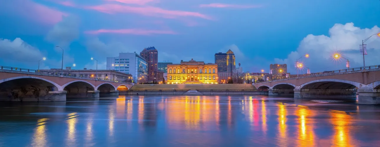 Evening cityscape with illuminated historic building and bridges reflecting on calm river.